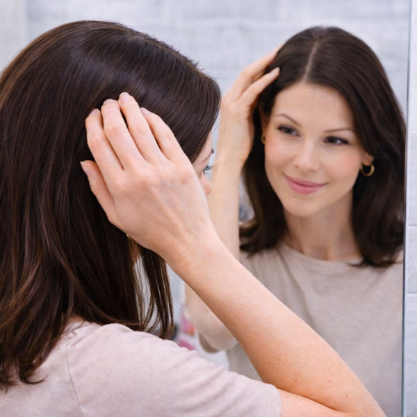 женщина поправляет прическу перед зеркалом после маскировки седины